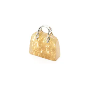 Nahaufnahme eines goldenen Natursteinanhängers in Handtaschenform mit silbernen Metallgriffen
