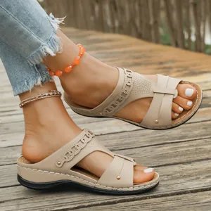 Detailed side view of beige wedge sandals with laser-cut patterns on wooden deck