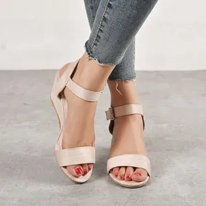 Close-up view of beige suede wedge sandals with an adjustable ankle strap buckle