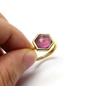 Detail view of a hexagonal purple crystal ring with a gold adjustable band held by hand
