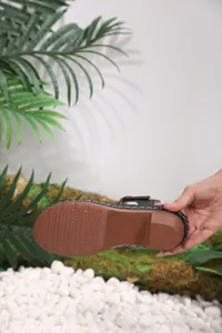 Detail of the non-slip brown rubber sole on a black women's sandal with white stitching.