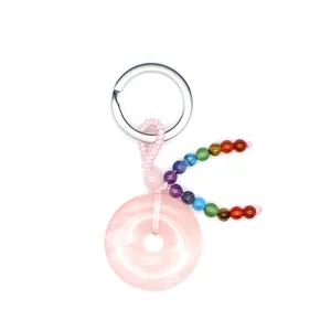 Detail van rozenkwarts sleutelhanger met zeven chakra kralen op witte achtergrond.