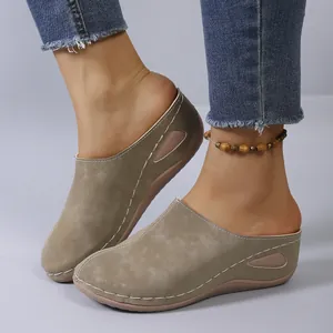 Detail view of khaki wedge mules featuring white contrast stitching and soft suede texture