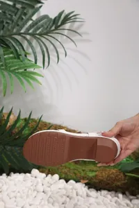 Detail view of anti-slip brown textured sole and sturdy block heel of white sandal