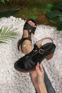 Close-up of black T-strap sandals with thick heels on a white pebble background