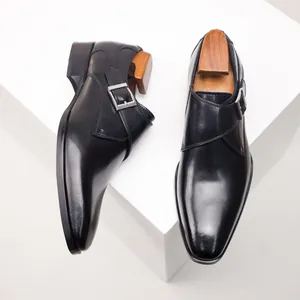 Detailed top-down view of black leather monk strap dress shoes on a white platform