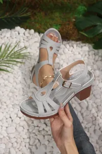 Detail view of grey chunky heel sandals with hollow-out design on white stone background