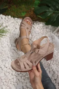 Detailed view of women's beige T-strap block heel sandals displayed on white pebbles