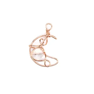 Close-up of hand-woven rose gold wire crescent moon pendant with natural clear stone.