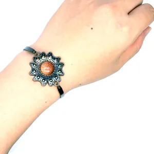 Klassisches Bronze-Blumenarmband mit natürlichem Sandstein-Zentrum am Handgelenk.