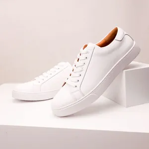 Detailed view of minimalist white leather men's sneakers on a white geometric prop.