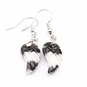 Detalle de pendientes de piedra natural con tallas únicas de alas en blanco y negro