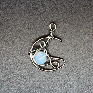 Detailed macro view of handmade silver wire-wrapped crescent moon pendant with a blue opal stone
