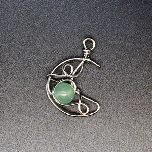 Close-up detail of handmade wire-wrapped crescent moon pendant with green stone.