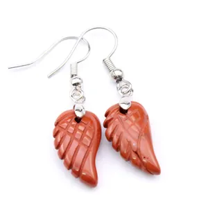 Detalle de pendientes de ala de ángel tallados en piedra natural roja