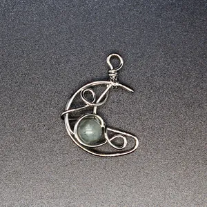 Detailed close-up of a handmade wire-wrapped silver moon pendant with a natural stone center