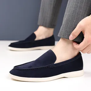 Side view of men's navy blue suede loafers worn with striped trousers on a white floor.