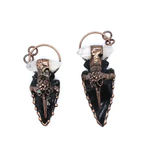 Detail view of two handmade obsidian arrowhead pendants with crystal and crow skull accents.
