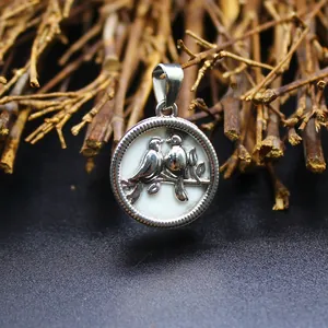 Détail d'un pendentif rond argenté avec deux oiseaux sur une base en pierre naturelle blanche.