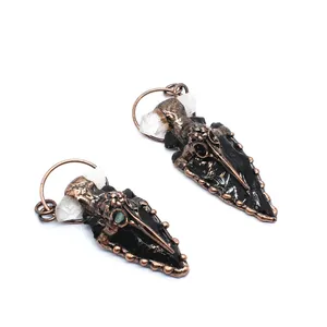 Close-up detail of obsidian crystal arrowhead pendant with vintage copper raven skull motif