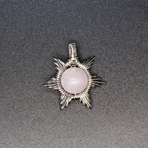 Macro detail of a handmade wire-wrapped pink stone sun pendant with silver finish