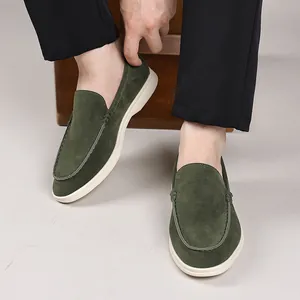Close-up of olive green suede loafers on a model wearing black trousers