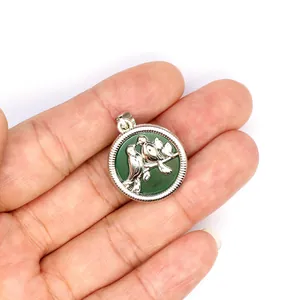 Vue détaillée d'un pendentif oiseau en argent avec pierre naturelle verte tenu en main.