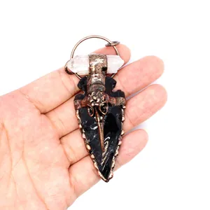 Macro view of gothic crow skull obsidian arrowhead pendant with clear quartz crystal point