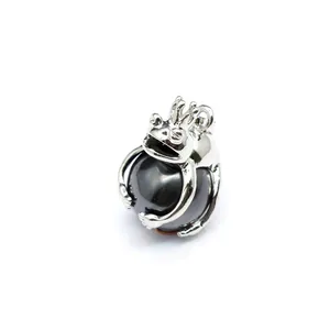 Macro view of a polished silver frog prince pendant holding a smooth dark hematite bead
