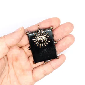 Détail d'un visage de soleil en bronze sur un pendentif en pierre noire rectangulaire.