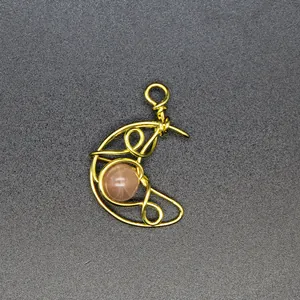 Close-up detail of hand-woven gold wire crescent moon pendant with peach sunstone bead