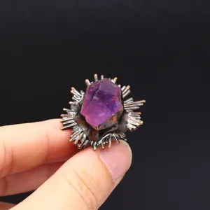 Detalle de un anillo vintage con una piedra natural morada sostenida por dedos en fondo negro.
