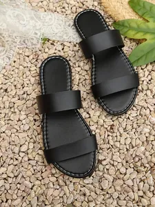Detailed view of black double-strap women's slides with white stitching on pebbles