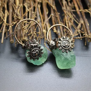 Detailed macro shot of raw green crystal pendants featuring antique bronze sun face charms.