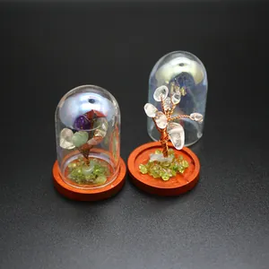Close-up of mini crystal tree of life with natural stones inside a clear glass dome.