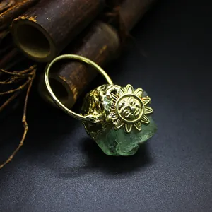 Macro detail of natural green crystal raw stone pendant with golden sun face engraving