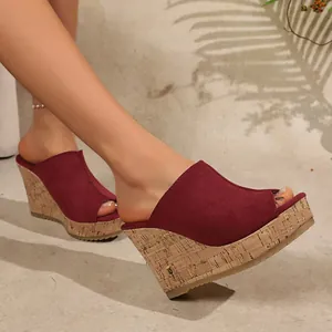 Detailed side view of elegant burgundy suede peep-toe wedge mules worn on model feet.