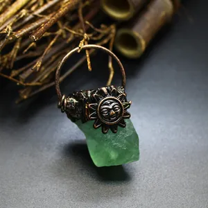 Macro detail of bohemian sun face bronze pendant featuring a green raw crystal stone