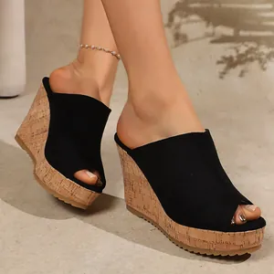 Detailed on-foot view of black suede peep-toe wedge sandals with cork platform heel