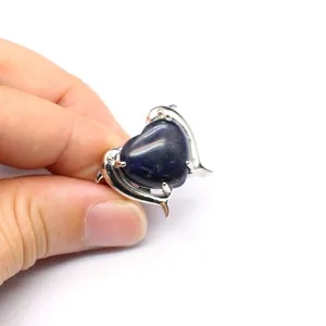 Dettaglio di un anello in ametista a forma di cuore con due delfini in argento tenuto in mano