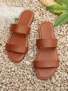 Detailed top view of brown faux leather two-strap slide sandals on a rustic pebble background