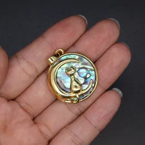 Detailansicht eines goldenen Anhängers mit Katze und Mond sowie echter Abalone-Muschel.