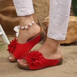 Detailed view of red wedge platform sandals with a large decorative flower on beach sand