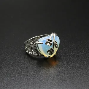 Macro view of a silver heart-shaped opal ring with intricate flower and leaf details.