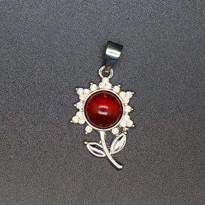 Detailaufnahme eines silbernen Blumenanhängers mit einem roten Stein und Kristallen