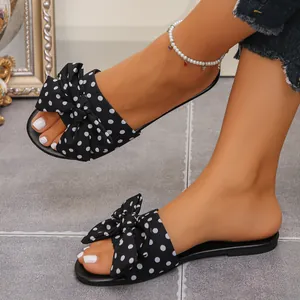 Detailed shot of black and white polka dot flat slides with decorative bow on model feet