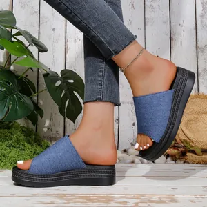 Side view of women's blue denim platform slides with thick black soles on wooden floor
