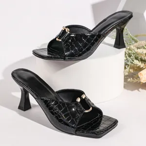 Macro view of crocodile texture and gold hardware on black square-toe heel sandals.