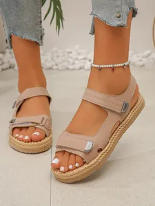 Dettaglio di sandali beige con zeppa, cinturini in velcro e suola intrecciata a mano