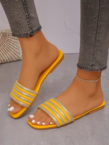 Dettaglio di eleganti sandali bassi gialli con cinturini in strass indossati ai piedi